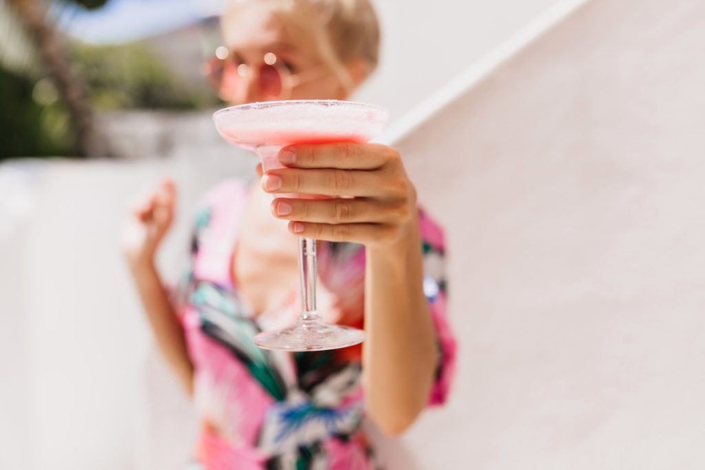 Portrait of elegant lady in bright dress with her hand in focus. Photo of magnificent woman with tanned skin with glass of cocktail on foreground.